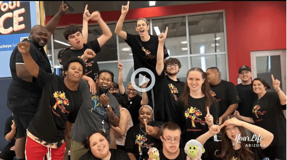 This is another rendering of proposed changes to The Opportunity Tree's facilities. It features a multi-stall restroom with light-colored wooden walls and doors, and a large multi-panel window behind the stalls. It has a white stone countertop and two handwashing stations are visible.